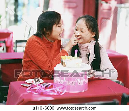 Stock Photograph - Young woman applying cake on another woman's nose. Fotosearch