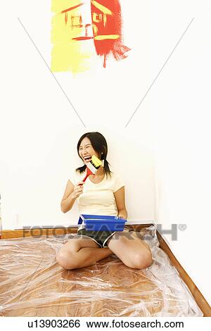 Stock Photograph - Young woman holding a paintbrush and laughing. Fotosearch