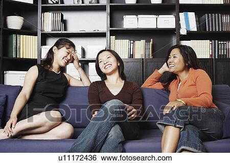 Stock Photograph - Close-up of a mid adult woman sitting with two young women on a couch smiling. Fotosearch