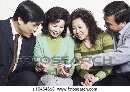 Stock Image - Close-up of two mature couples sitting together looking at a mobile phone. Fotosearch