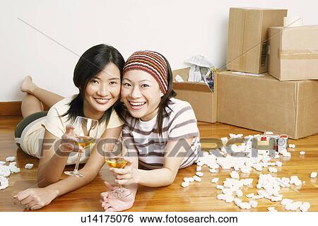 Stock Photograph - Portrait of two young women lying on the floor and holding glasses of whiskey. Fotosearch