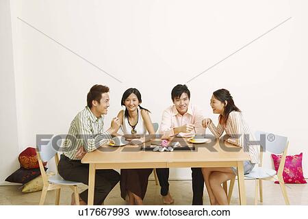 Stock Image - Two young couples eating noodles and smiling. Fotosearch