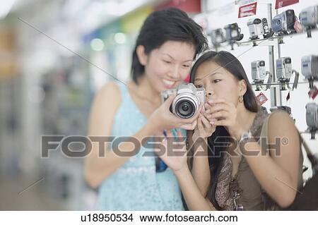 Two young women holding a camera View Large Photo Image Picture - Two young women holding a camera. Fotosearch
