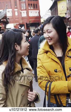 Stock Image - Two young women looking at each other smiling in a street market. Fotosearch
