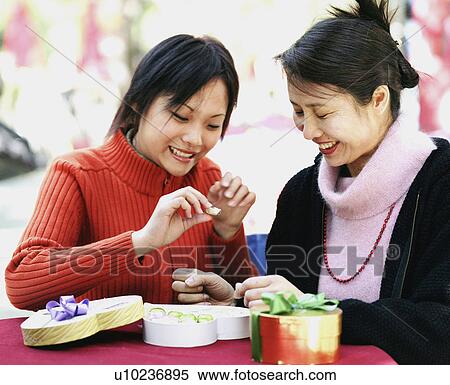 Stock Photography - Two young women seated at a table and holding a candy. Fotosearch