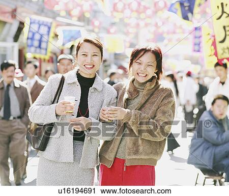 Stock Image - Two young women standing holding cups. Fotosearch