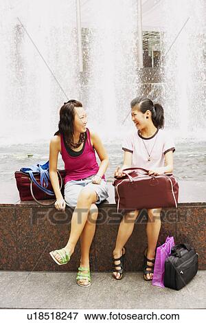 Two young women talking near a fountain View Large Photo Image Stock Photo - Two young women talking near a fountain. Fotosearch
