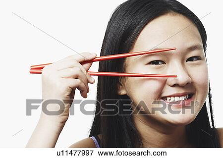 Stock Photo - Portrait of a teenage girl looking through chopsticks. Fotosearch