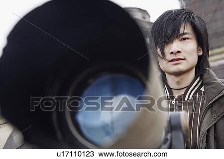 Stock Image - Close-up of a telescope in front of a young man. Fotosearch