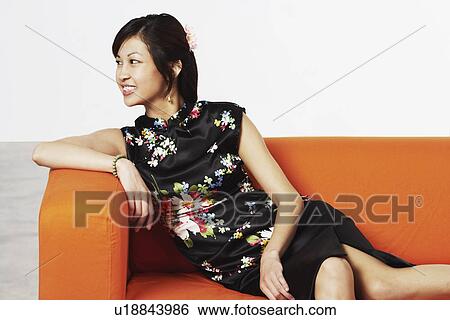Stock Photograph - Close-up of a young woman sitting on a couch smiling. Fotosearch