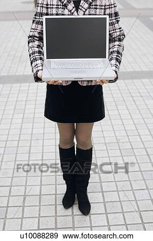Stock Photo - Low section view of a woman holding a laptop. Fotosearch