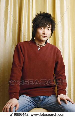 Stock Image - Portrait of a young man sitting on a stool. Fotosearch