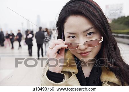 Portrait of a young woman holding sunglasses over her eyes View Large Photo Image Stock Image - Portrait of a young woman holding sunglasses over her eyes. Fotosearch