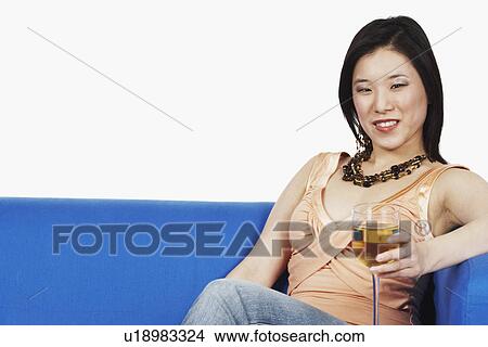 Picture - Portrait of a young woman sitting on a couch holding a glass of red wine. Fotosearch