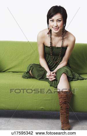 Stock Image - Portrait of a young woman sitting on a couch smiling. Fotosearch