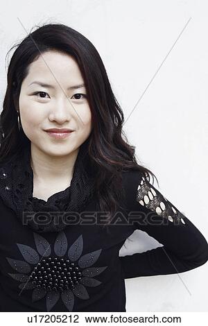 Stock Image - Portrait of a young woman standing with her hands behind her back smiling. Fotosearch