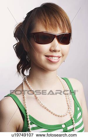 Stock Photo - Portrait of a young woman wearing sunglasses and smiling. Fotosearch