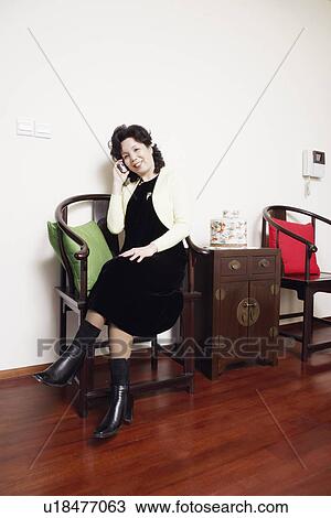 Stock Image - Mature woman sitting on a chair talking on a mobile phone. Fotosearch