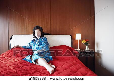 Picture - Portrait of a mature woman relaxing on the bed smiling. Fotosearch