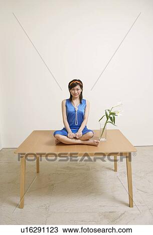 Stock Image - Portrait of a young woman sitting on a table and smiling. Fotosearch