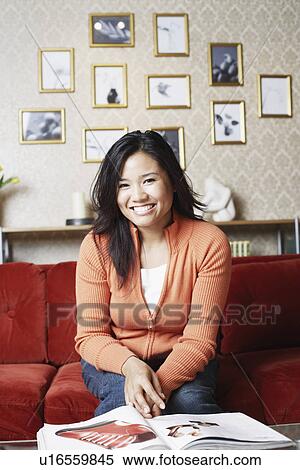 Stock Photography - Portrait of a young woman sitting on a couch smiling. Fotosearch