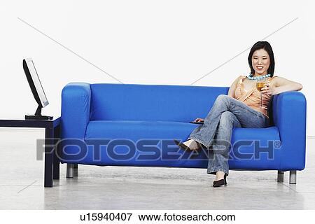 Stock Photo - Young woman holding a glass of red wine sitting on a couch. Fotosearch