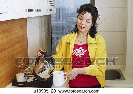 Stock Image - Close-up of a mature woman pouring coffee into a cup. Fotosearch