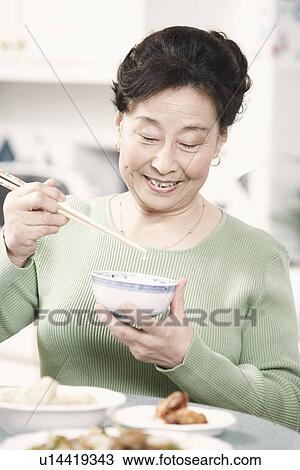 Stock Image - Close-up of a senior woman holding chopsticks and a bowl. Fotosearch