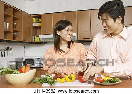 Stock Image - Close-up of a young couple cutting vegetables at a kitchen counter. Fotosearch