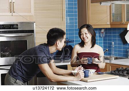 Stock Image - Close-up of a young couple holding cups in the kitchen. Fotosearch