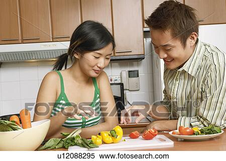 Stock Photography - Close-up of a young couple looking at sliced vegetables on a cutting board at a kitchen counter. Fotosearch