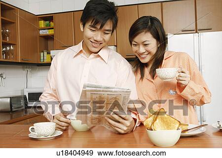 Close-up of a young couple reading a newspaper at a kitchen counter View Large Photo Image Stock Photo - Close-up of a young couple reading a newspaper at a kitchen counter. Fotosearch