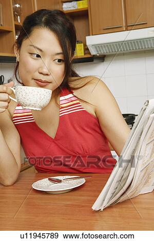 Close-up of a young woman reading a newspaper at a kitchen counter View Large Photo Image Stock Photo - Close-up of a young woman reading a newspaper at a kitchen counter. Fotosearch