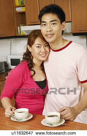 Stock Photo - Portrait of a mid adult man and a young woman holding cups of tea at a kitchen counter. Fotosearch
