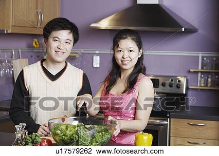 Stock Image - Portrait of a young man standing with a mid adult woman in the kitchen. Fotosearch