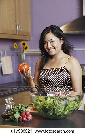 Portrait of a young woman holding a tomato in the kitchen View Large Photo Image Stock Image - Portrait of a young woman holding a tomato in the kitchen. Fotosearch