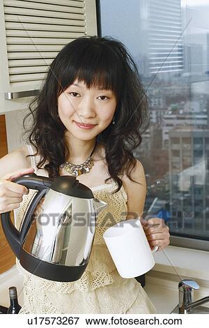 Portrait of a young woman holding a kettle and a mug View Large Photo Image Stock Photo - Portrait of a young woman holding a kettle and a mug. Fotosearch