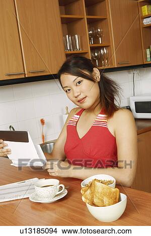 Portrait of a young woman holding an envelope at a kitchen counter View Large Photo Image Picture - Portrait of a young woman holding an envelope at a kitchen counter. Fotosearch