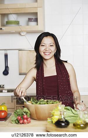 Stock Photo - Portrait of a young woman preparing food in the kitchen smiling. Fotosearch