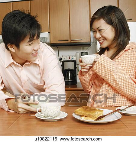 Stock Photograph - Young couple having breakfast and looking at each other at a kitchen counter. Fotosearch
