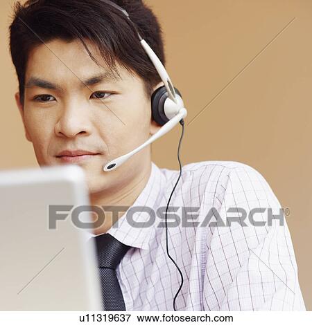 Close-up of a male customer service representative talking on a headset and using a laptop View Large Photo Image Stock Photo - Close-up of a male customer service representative talking on a headset and using a laptop. Fotosearch