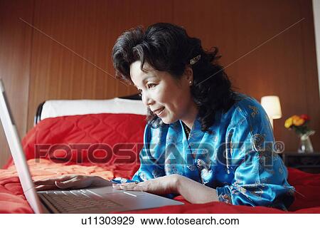 Close-up of a mature woman sitting on the bed using a laptop View Large Photo Image Stock Photo - Close-up of a mature woman sitting on the bed using a laptop. Fotosearch