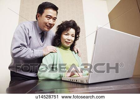 Stock Image - Low angle view of a mature couple using a laptop. Fotosearch