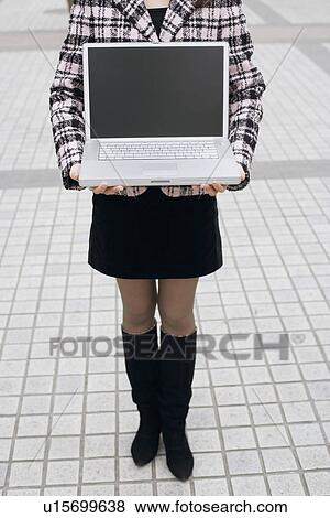 Low section view of a woman holding a laptop View Large Photo Image Stock Photo - Low section view of a woman holding a laptop. Fotosearch