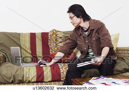 Mid adult man sitting on a couch and using a laptop View Large Photo Image Stock Image - Mid adult man sitting on a couch and using a laptop. Fotosearch