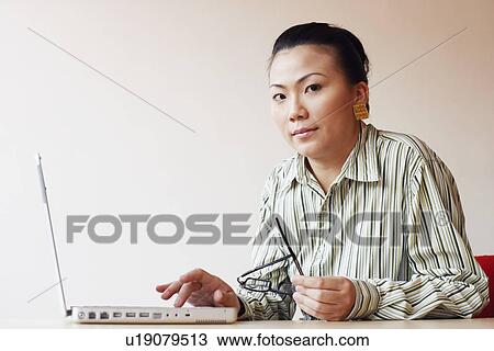 Stock Image - Portrait of a businesswoman sitting in an office and using a laptop. Fotosearch