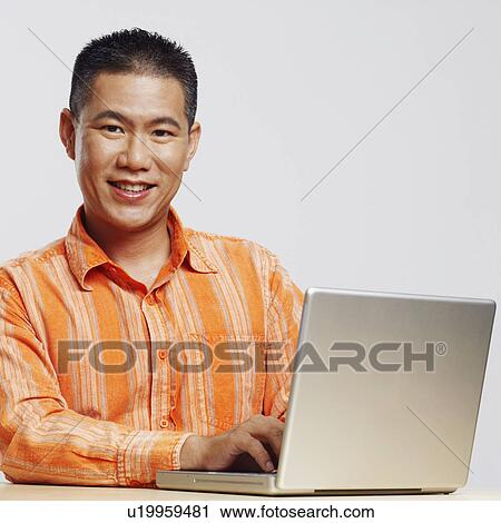 Stock Image - Portrait of a mid adult man using a laptop and smiling. Fotosearch