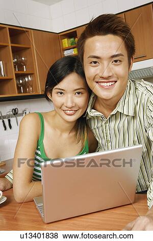 Stock Photo - Portrait of a young couple smiling in front of a laptop at a kitchen counter. Fotosearch