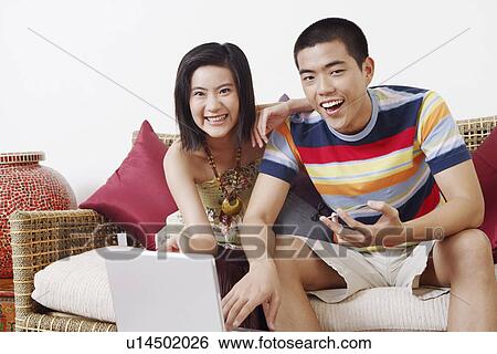 Stock Photograph - Portrait of a young man holding a credit card and using a laptop with a young woman sitting beside him. Fotosearch