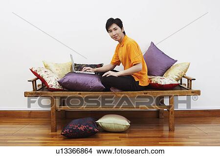 Picture - Portrait of a young man sitting on a bench and using a laptop. Fotosearch